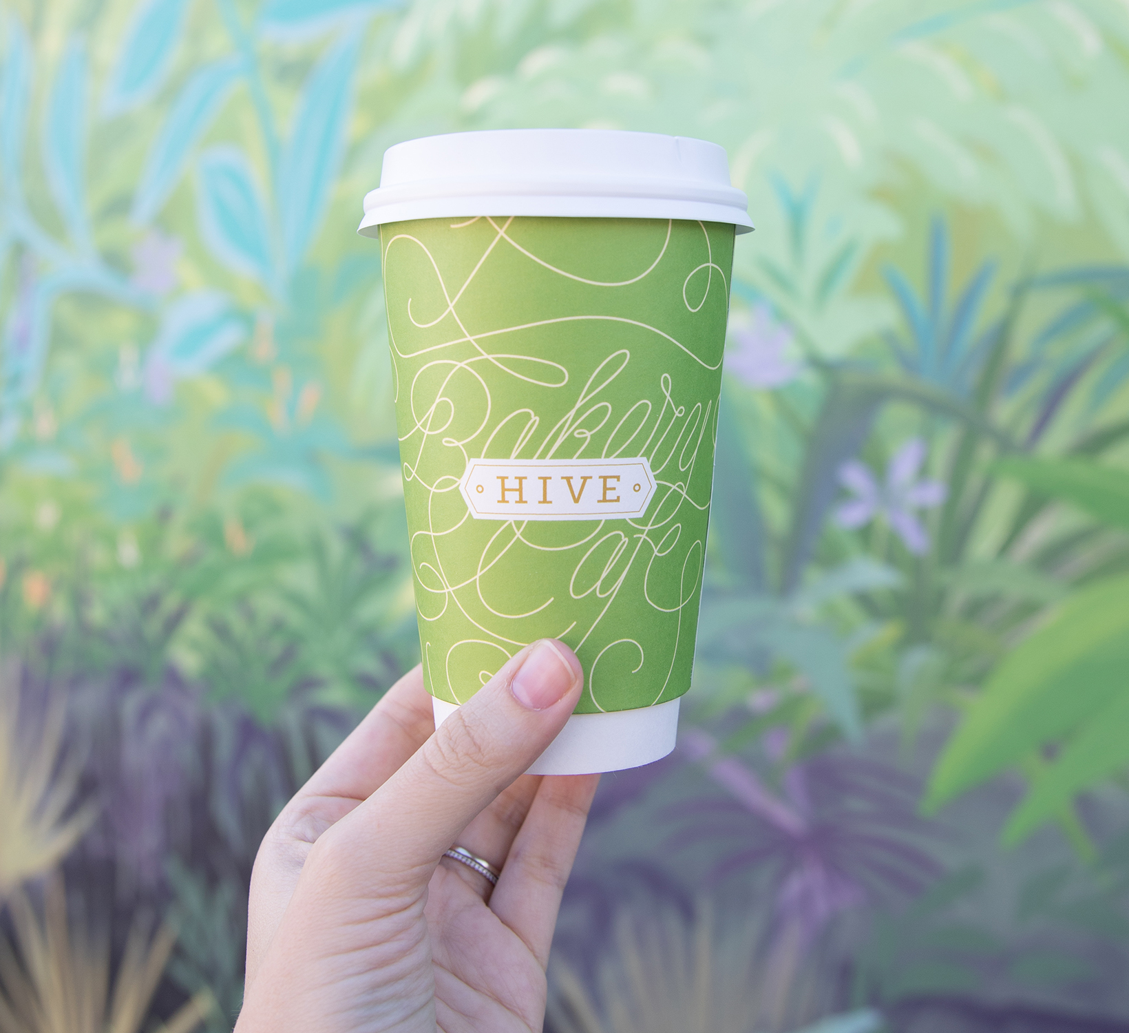 image of hive to go coffee cup against hive tropical mural wall